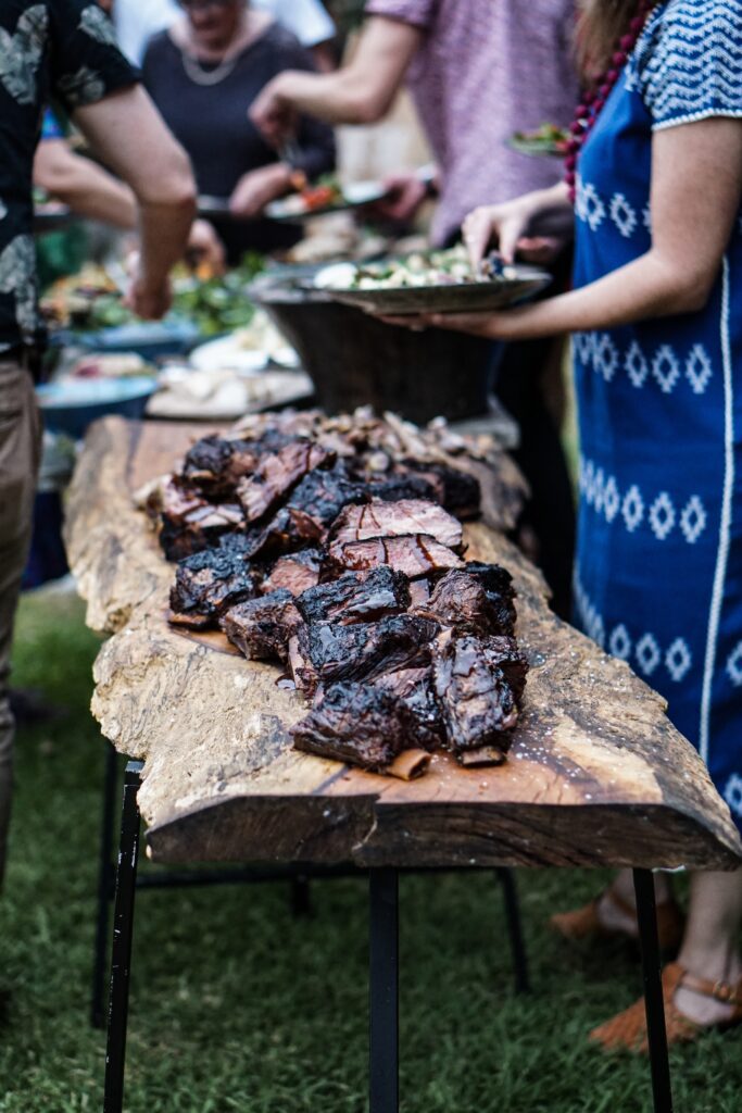 Guests at an outdoor party choosing delicious main course and side dishes from a wooden table from a local caterer.